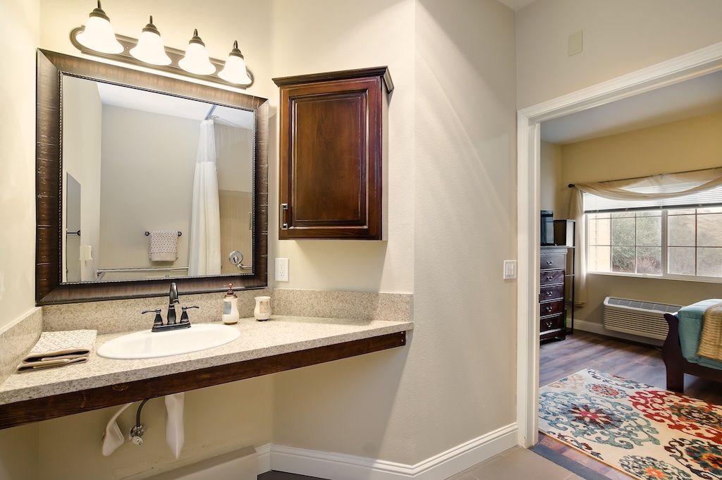 A well-lit bathroom features a vanity with a sink, mirror, and wooden cabinet.