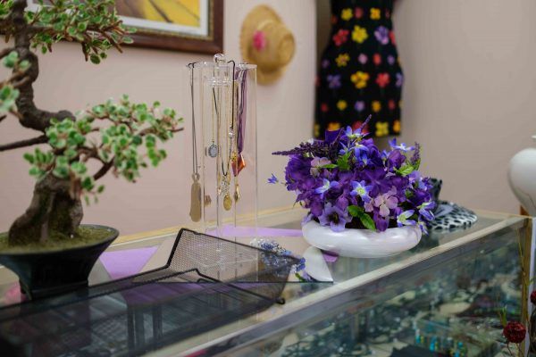 A boutique display featuring necklaces, a vibrant dress, and a bowl of purple flowers.
