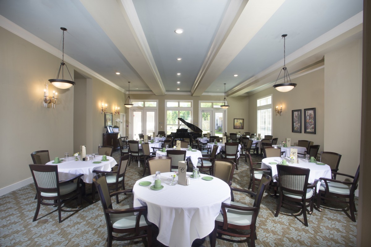 Elegant dining room with round tables, chairs, and a grand piano.