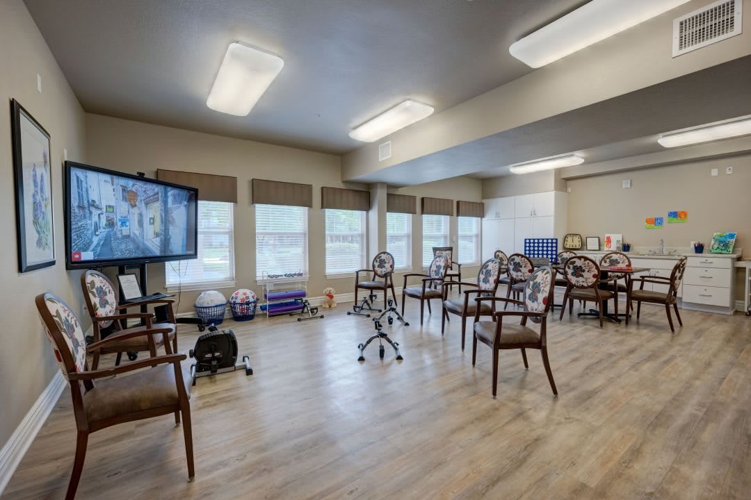 A well-lit classroom setup with chairs, a television, and large windows.