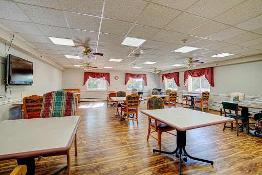 A spacious and well-lit dining area featuring wooden floors, tables, and chairs with ceiling fans.