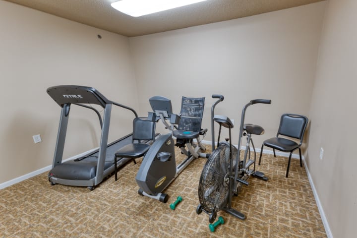 A small fitness room with various exercise equipment, including a treadmill and stationary bikes.