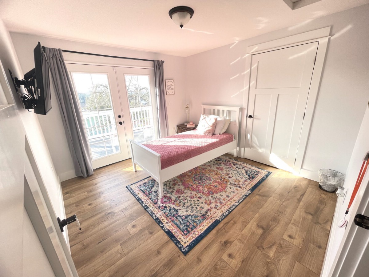 A bright, minimalist bedroom with a single bed and a colorful rug on a wooden floor.