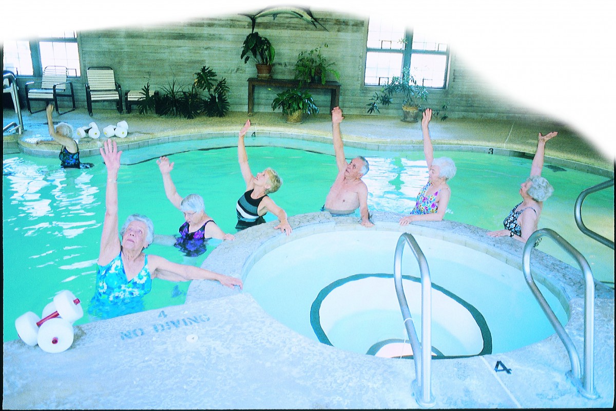 A group of elderly women participating in a water aerobics class in an indoor swimming pool.