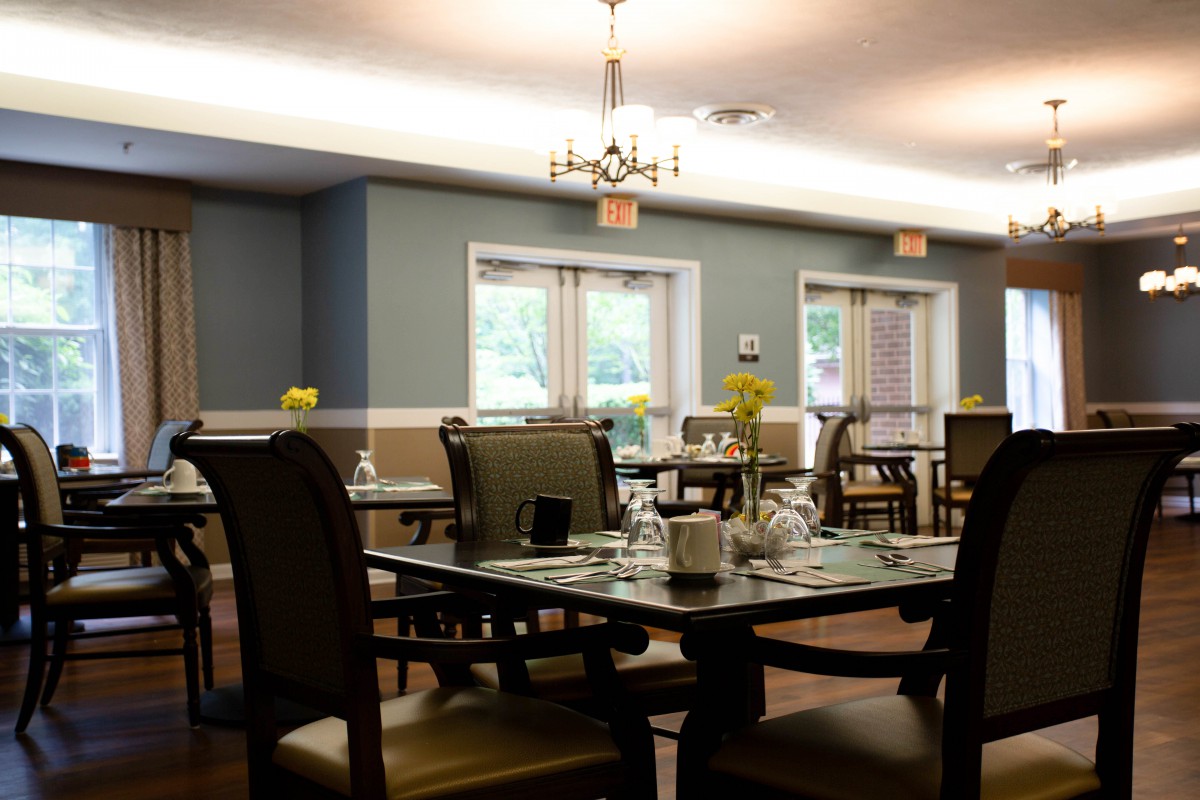 A cozy dining room with neatly arranged tables and chairs, illuminated by warm lighting.