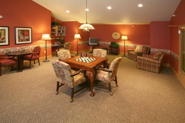 A cozy basement game room featuring a chessboard on a wooden table surrounded by chairs, with warm lighting and comfortable seating.