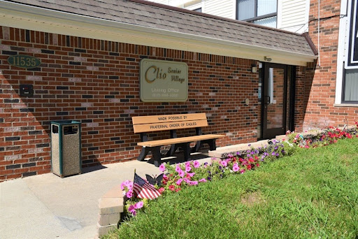 A welcoming entrance with a bench and flowers in front of a brick building.