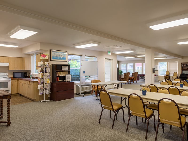 A spacious and bright common room with multiple tables and chairs arranged for social gatherings.