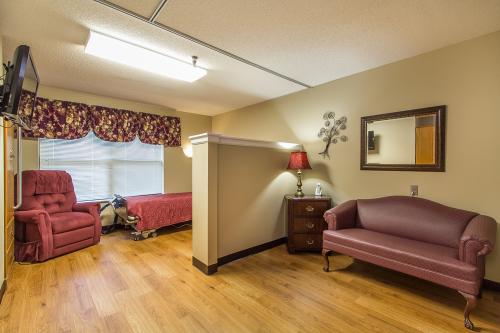 A cozy patient room in a care facility, featuring two beds and comfortable seating.