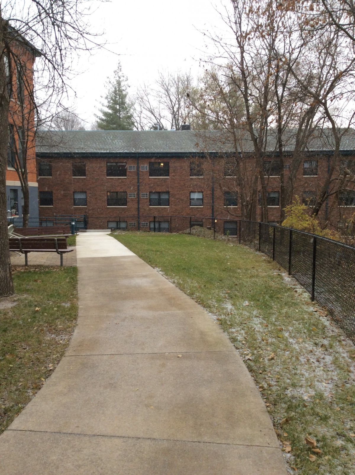 A view of a brick apartment building with a concrete pathway lined by grass and trees in winter.