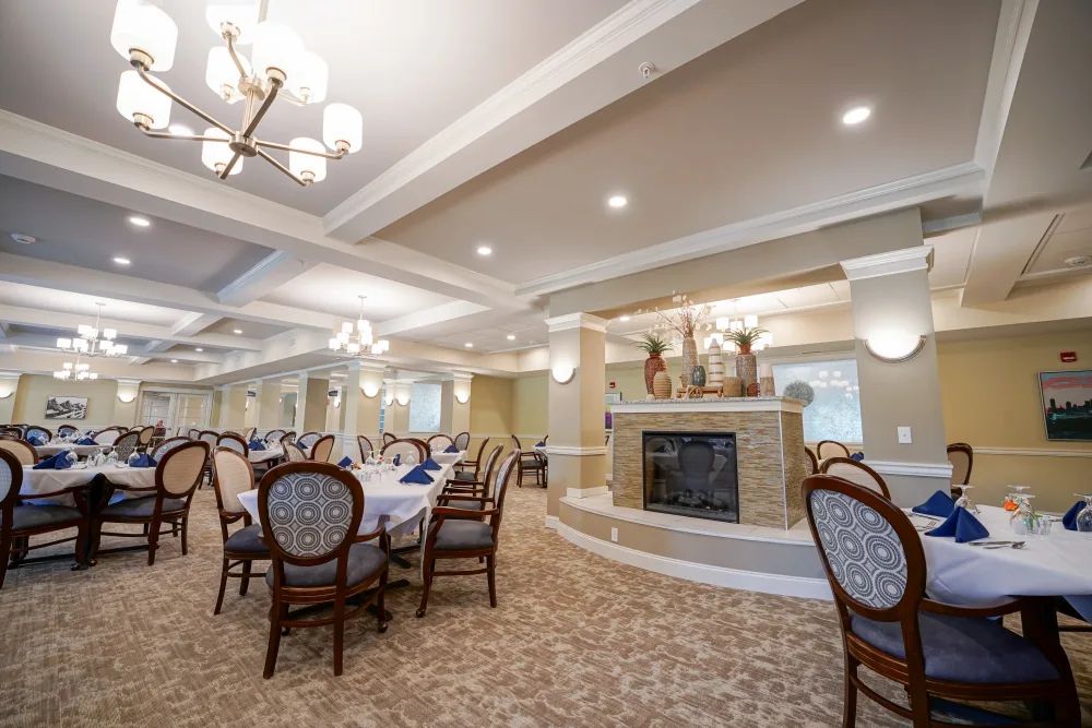 A spacious dining room with elegant chandeliers, a fireplace, and neatly arranged tables and chairs.
