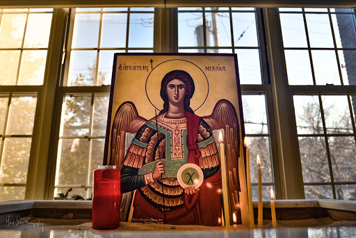 An icon of an angel displayed by a window, illuminated by natural light, accompanied by candles.
