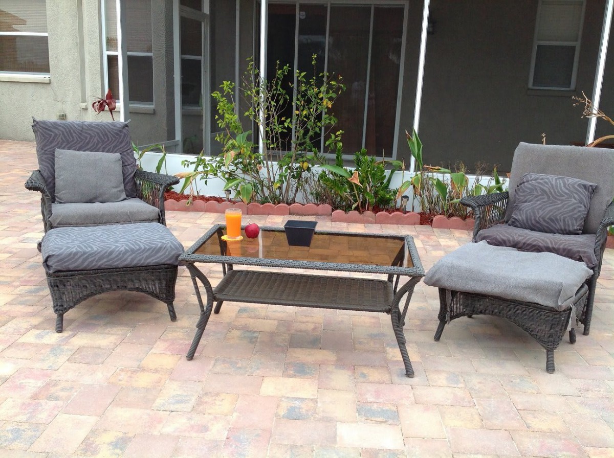 A cozy patio setup with two cushioned chairs and a glass-top table surrounded by greenery.