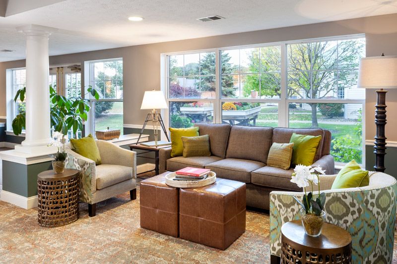A cozy living room featuring a comfortable brown sofa, an armchair, and a coffee table under large windows with outdoor views.
