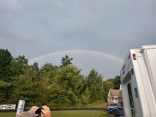 A beautiful rainbow arches over a lush green landscape, contrasting with the gray clouds above.