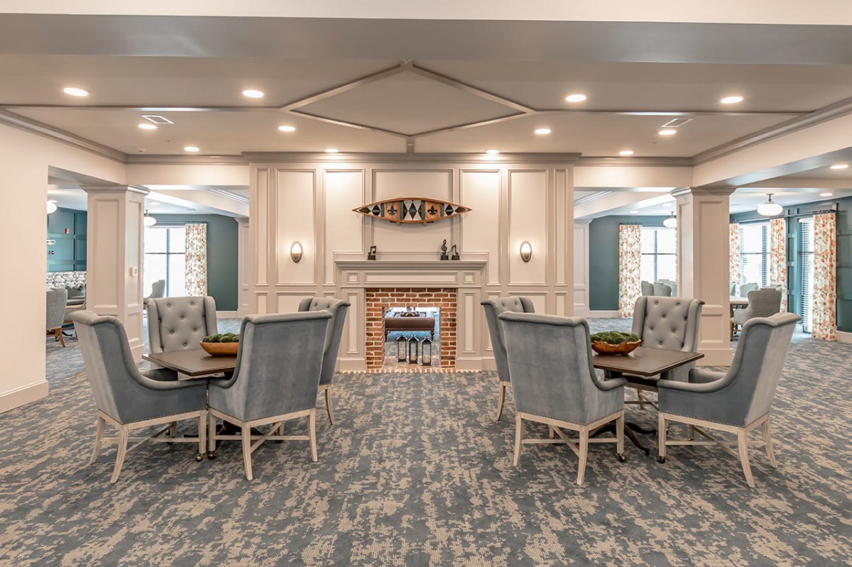 A spacious and elegantly decorated room featuring several tables and chairs arranged symmetrically around a central fireplace.