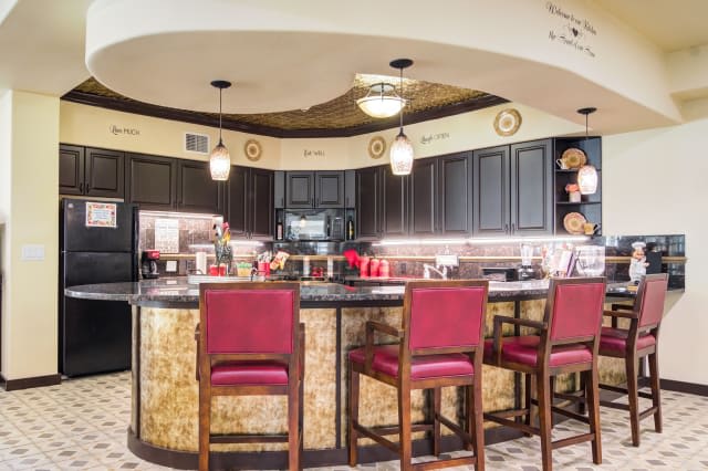 A modern kitchen with a bar area featuring red chairs and black cabinets.
