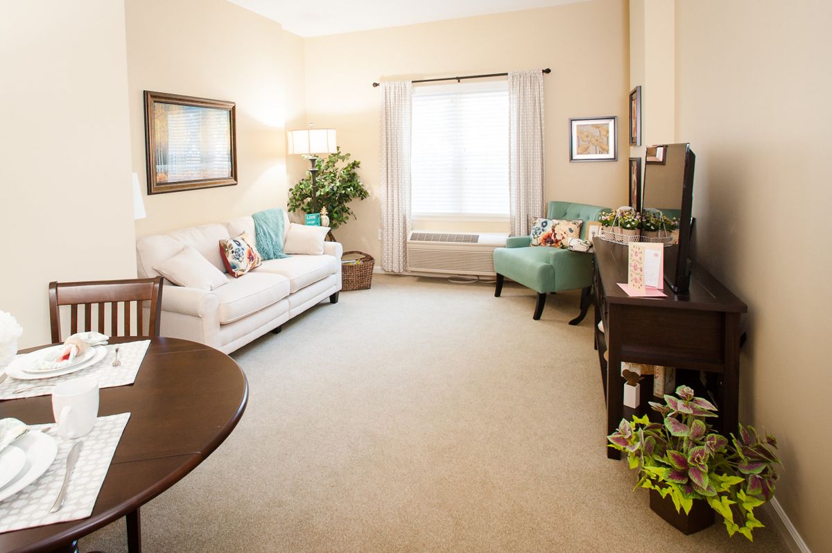 A cozy and well-lit living room with a sofa and armchair, complemented by decorative elements and a large window.