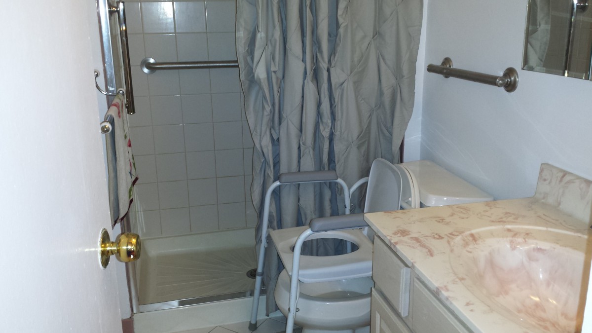 A bathroom with a shower equipped for accessibility, featuring a safety chair and grab bars.