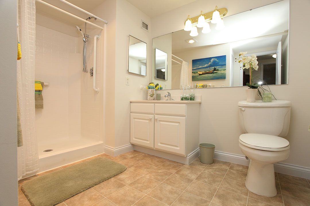 A well-lit bathroom with a shower, vanity, mirror, and toilet.