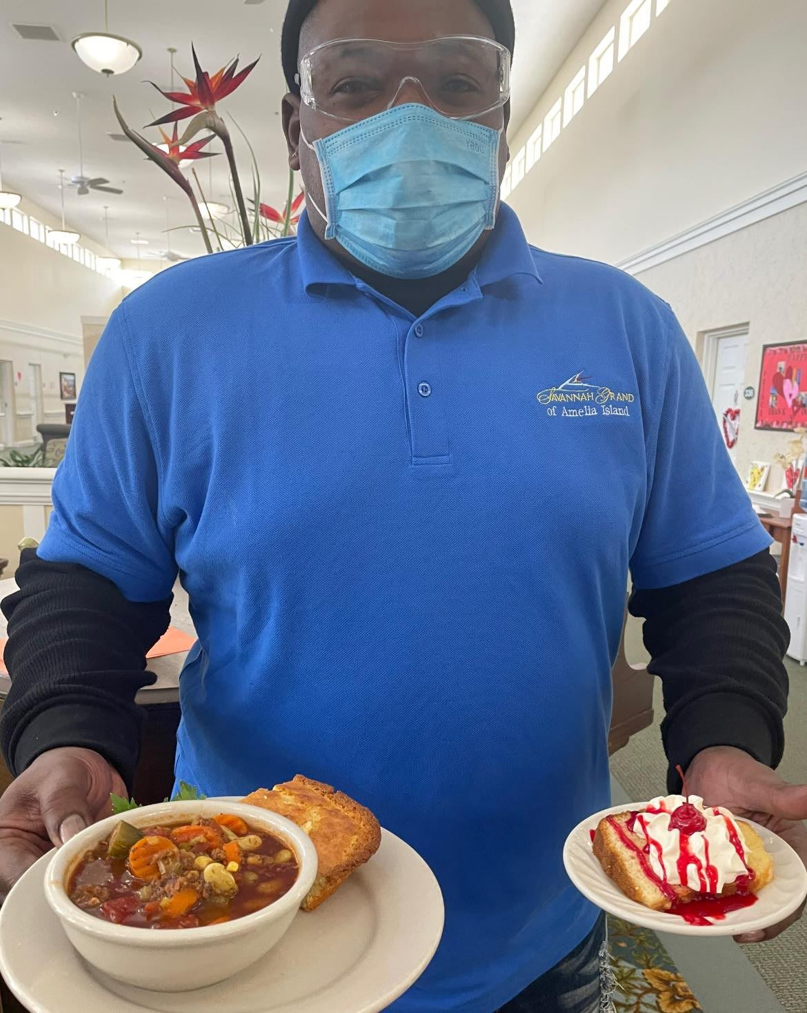 A person in a blue shirt holding two plates with food and dessert, inside a restaurant.