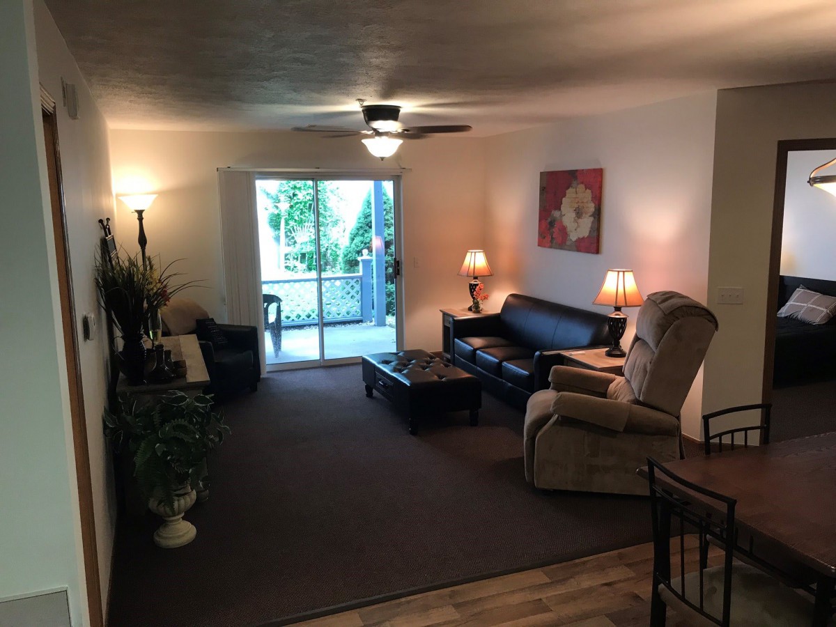 A cozy living room with a sofa, recliner, lamps, and a ceiling fan, featuring a sliding door leading to an outdoor space.