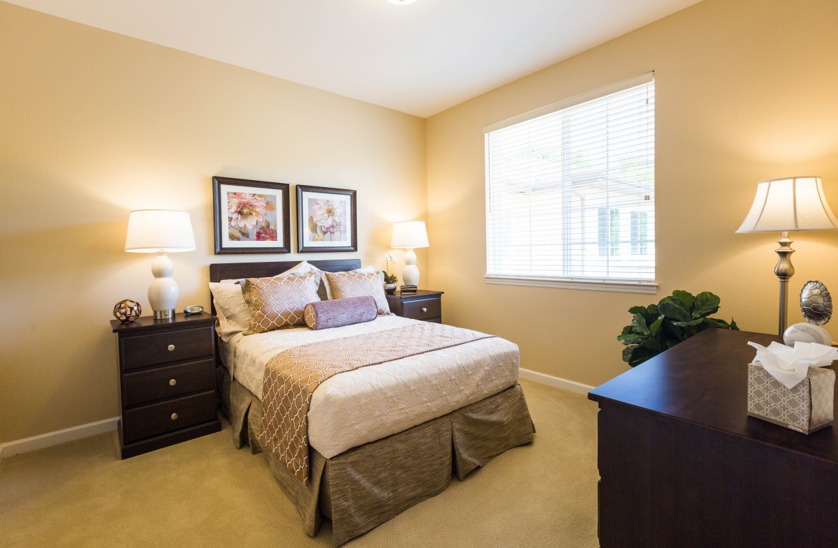 A cozy bedroom interior with a neatly made bed, decorative pillows, and framed artwork above the headboard.