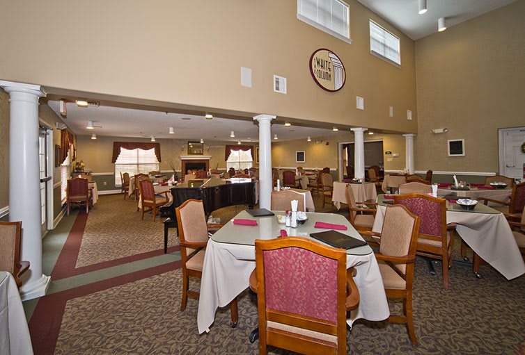 A spacious dining area with neatly arranged tables and chairs, featuring a carpeted floor and large windows.