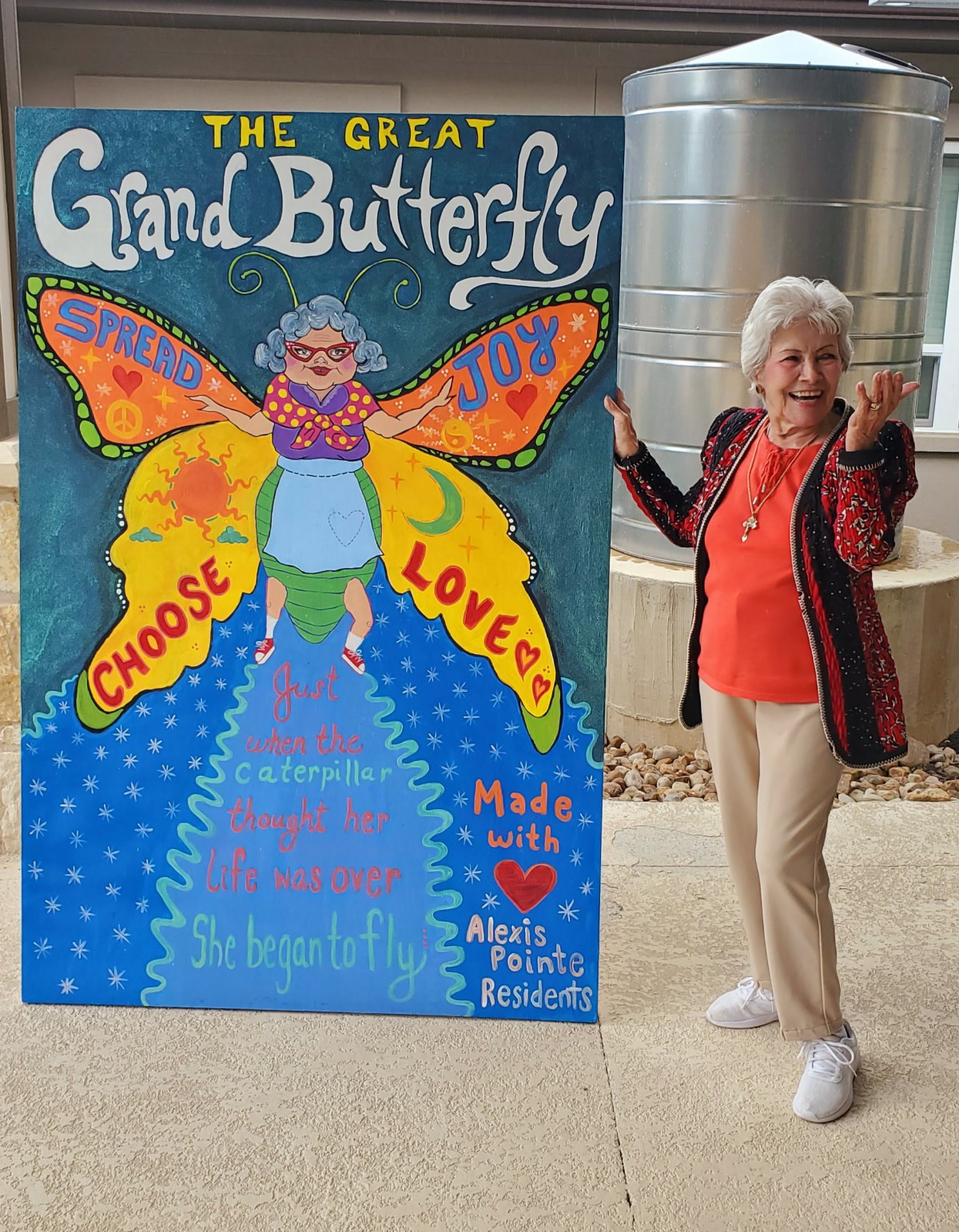 A woman stands next to a colorful butterfly-themed artwork titled 'The Great Grand Butterfly'.