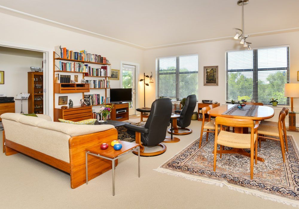 A cozy living room with a bookshelf, sofa, chairs, and dining area.