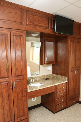 A modern bathroom vanity featuring wooden cabinets and a granite countertop, equipped with a mirror and a television.