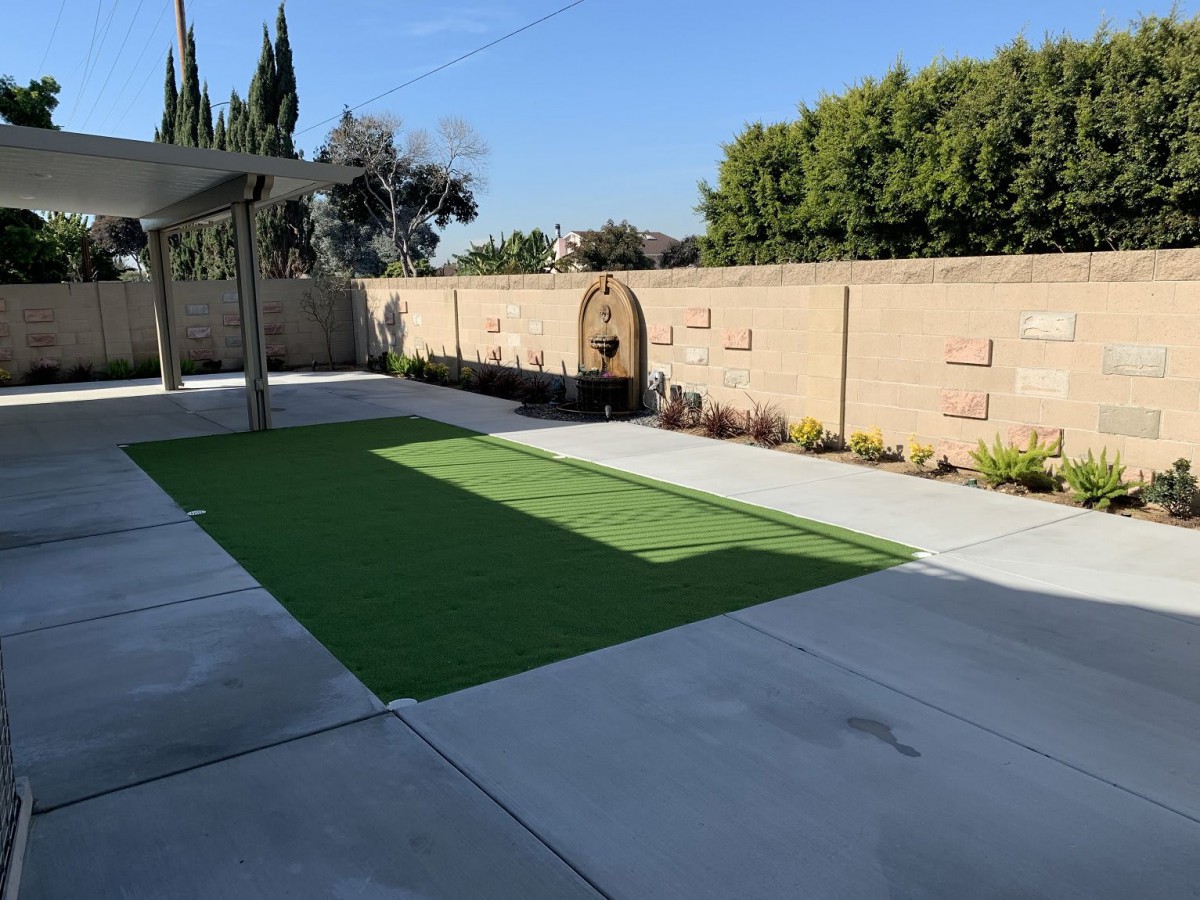 A well-maintained backyard with artificial grass and concrete patio, surrounded by a garden wall.