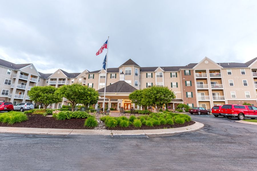 A view of a hotel exterior with a circular driveway, flags, and landscaped greenery.