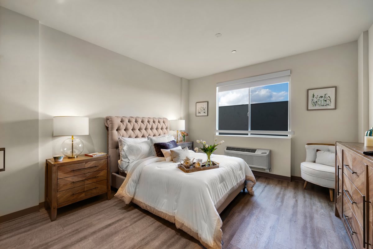 A modern and stylish bedroom with a comfortable bed, wooden furniture, and ample natural light.