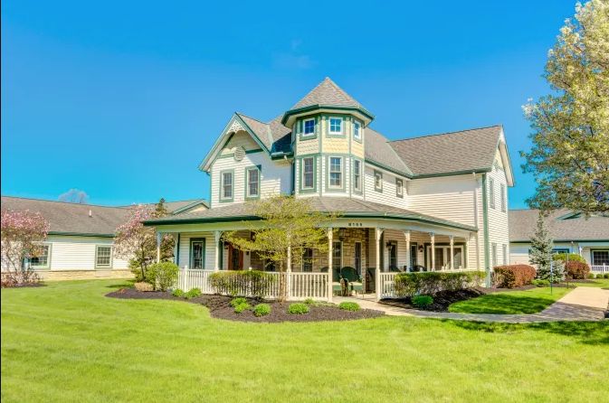 A beautiful Victorian-style house with a wraparound porch and a well-maintained lawn under a clear blue sky.