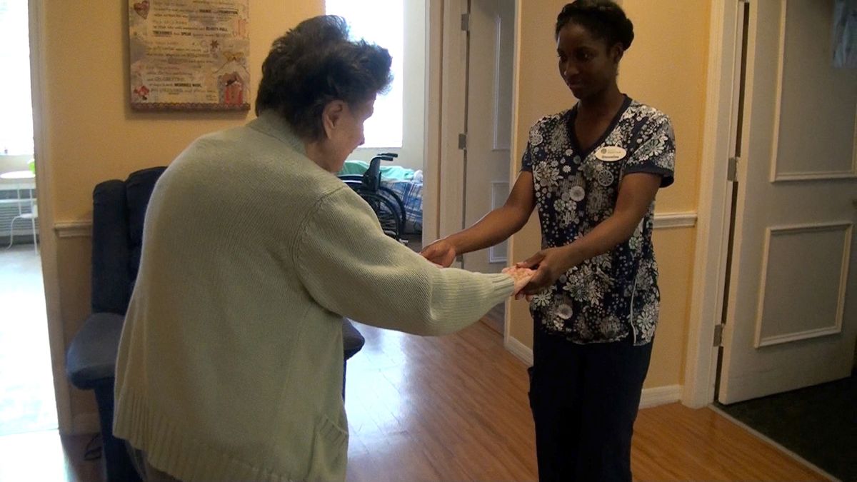 A caregiver assisting an elderly person with mobility exercises in a healthcare facility.