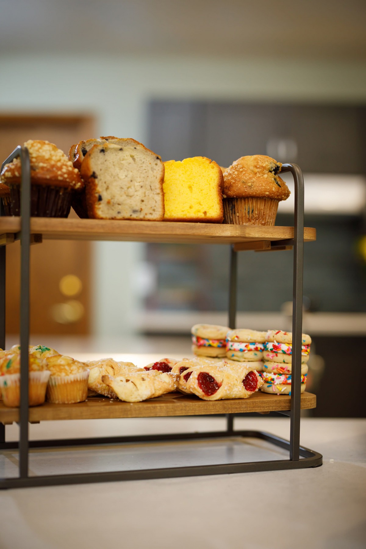 A two-tiered stand displaying a variety of baked goods, including muffins and slices of bread.