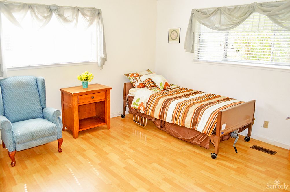 A cozy bedroom with a single bed, wooden flooring, and natural light from the windows.