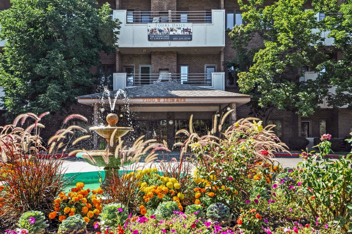 A vibrant garden with a fountain in front of a building.