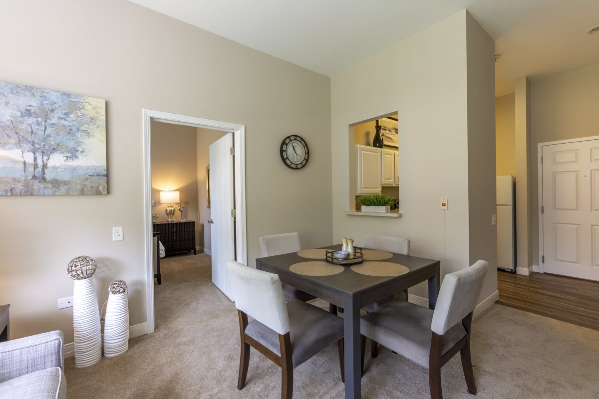 A modern dining room with a square table, cushioned chairs, and a wall clock.