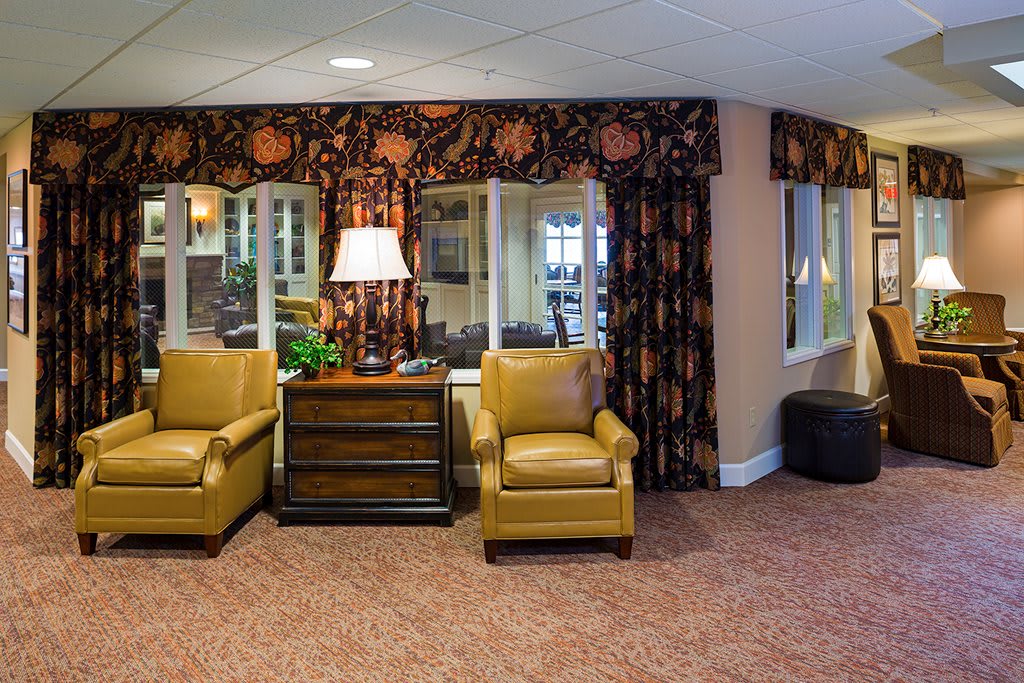 A cozy living room with two leather chairs, a lamp, and floral curtains.
