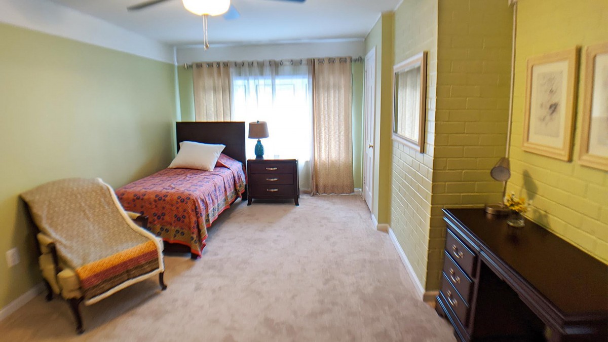A cozy bedroom with a single bed, bedside table, and natural light from a curtained window.