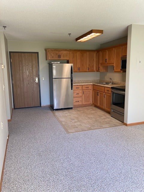 A compact apartment kitchen with wooden cabinets and stainless steel appliances.