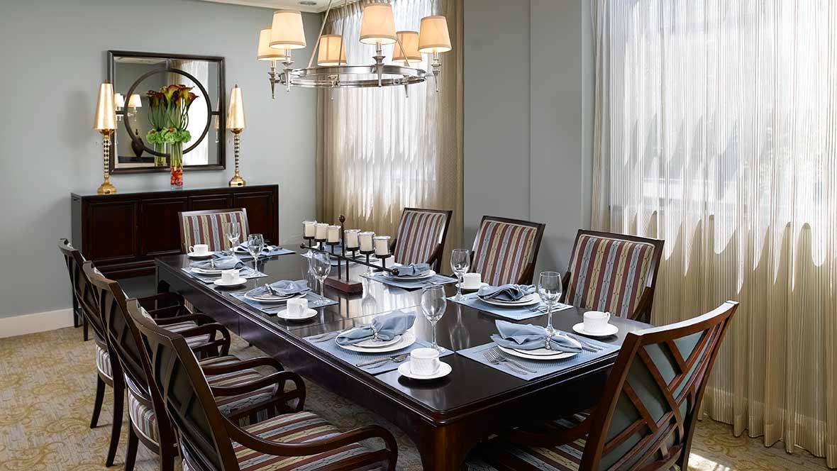 A beautifully set dining room with an elegant table arrangement and striped chairs, illuminated by a chandelier.
