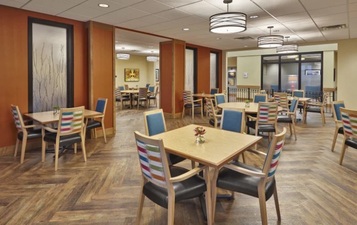A modern dining room with neatly arranged tables and colorful chairs, featuring elegant lighting fixtures.