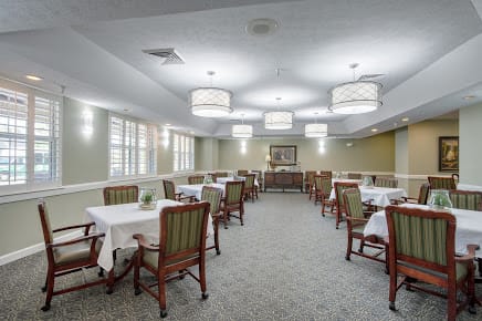 A spacious dining room with neatly arranged tables and chairs, accented by elegant lighting.