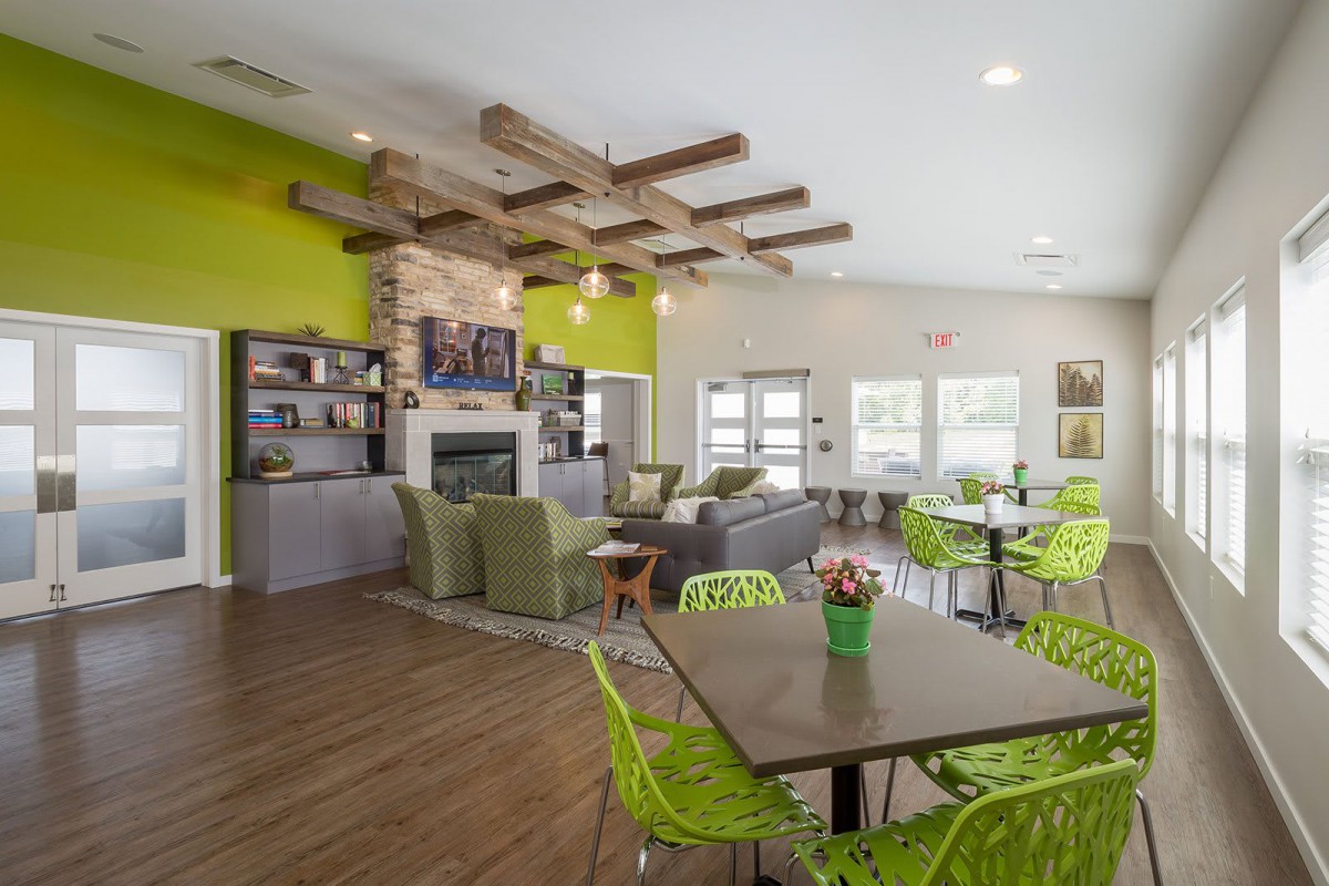 A modern interior living space with green accents, featuring a cozy seating area, wooden beam ceiling, and dining tables.