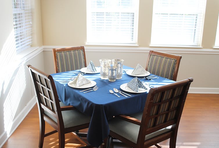 A dining table with a blue tablecloth and place settings for four in a sunlit room.