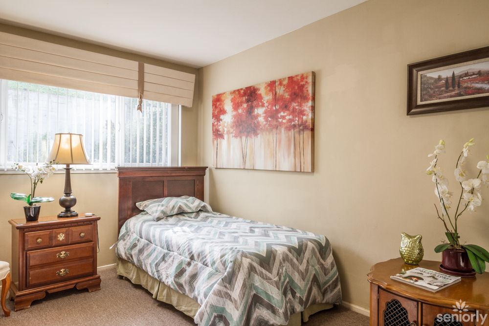 A cozy bedroom with a single bed, artwork on the wall, and a nightstand with a lamp.