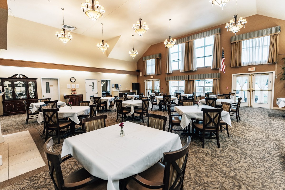 A spacious dining room with multiple tables covered in white tablecloths and elegant lighting.